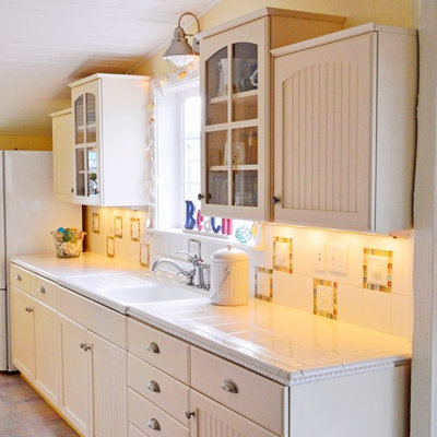 Inspiration for a small coastal galley vinyl floor enclosed kitchen remodel in Seattle with an integrated sink, recessed-panel cabinets, white cabinets, tile countertops, white backsplash, glass tile backsplash and white appliances
