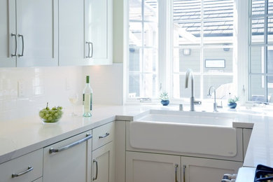 Kitchen - transitional u-shaped medium tone wood floor kitchen idea in Los Angeles with a farmhouse sink, shaker cabinets, white cabinets, quartz countertops, white backsplash, subway tile backsplash and paneled appliances