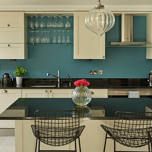 This is an example of a classic galley kitchen in Surrey with a submerged sink, shaker cabinets, beige cabinets, stainless steel appliances, an island, beige floors and black worktops.
