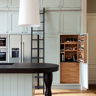 Photo of a victorian galley kitchen in London with an integrated sink, shaker cabinets, stainless steel appliances, medium hardwood floors, with island and blue cabinets.