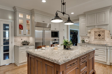 Inspiration for a large timeless light wood floor kitchen remodel in Baltimore with a farmhouse sink, raised-panel cabinets, granite countertops, beige backsplash, travertine backsplash, stainless steel appliances and an island