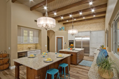 Example of a large trendy galley light wood floor and brown floor eat-in kitchen design in Phoenix with a drop-in sink, beaded inset cabinets, white cabinets, granite countertops, beige backsplash, stainless steel appliances and two islands