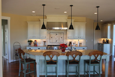Eat-in kitchen - large traditional dark wood floor eat-in kitchen idea in Other with a farmhouse sink, raised-panel cabinets, white cabinets, granite countertops, beige backsplash, stone tile backsplash, stainless steel appliances and an island