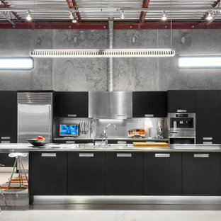 Design ideas for an industrial kitchen in Birmingham with an integrated sink, flat-panel cabinets, black cabinets, stainless steel benchtops, metallic splashback, stainless steel appliances, concrete floors and with island.
