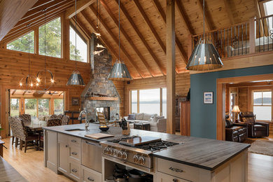 Rustic open plan kitchen in Burlington with recessed-panel cabinets, green cabinets, soapstone worktops, stainless steel appliances, light hardwood flooring and an island.