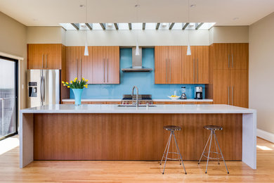 Open concept kitchen - mid-sized contemporary galley light wood floor open concept kitchen idea in San Francisco with an undermount sink, flat-panel cabinets, medium tone wood cabinets, quartz countertops, blue backsplash, glass sheet backsplash, stainless steel appliances and an island