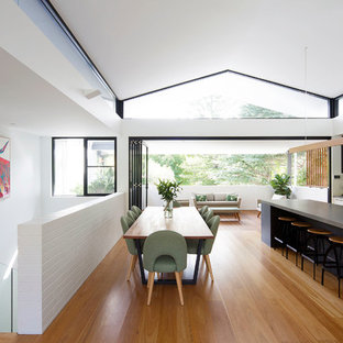 Inspiration for a mid-sized contemporary galley open plan kitchen in Sydney with an undermount sink, flat-panel cabinets, white cabinets, quartz benchtops, white splashback, glass sheet splashback, black appliances, medium hardwood floors, with island, brown floor and grey benchtop.