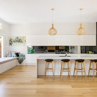 Design ideas for a contemporary l-shaped kitchen in Sydney with an undermount sink, flat-panel cabinets, white cabinets, mirror splashback, stainless steel appliances, light hardwood floors, with island, beige floor and white benchtop.