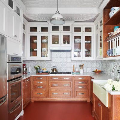 Mid-sized eclectic u-shaped red floor and concrete floor enclosed kitchen photo in Toronto with a farmhouse sink, shaker cabinets, medium tone wood cabinets, gray backsplash, ceramic backsplash, stainless steel appliances, no island, white countertops and solid surface countertops