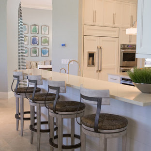 Large beach style l-shaped open plan kitchen in Miami with an undermount sink, recessed-panel cabinets, white cabinets, quartz benchtops, beige splashback, matchstick tile splashback, stainless steel appliances, ceramic floors, with island and beige floor.