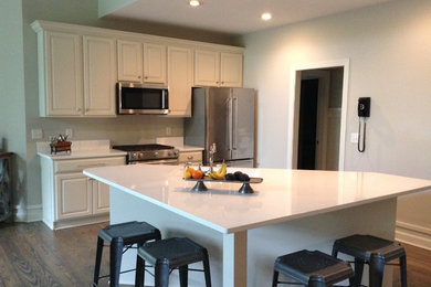 Inspiration for a small traditional open plan kitchen in Charlotte with a submerged sink, raised-panel cabinets, white cabinets, quartz worktops, white splashback, stainless steel appliances, medium hardwood flooring, an island and brown floors.