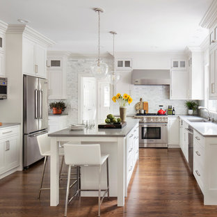 This is an example of a traditional u-shaped separate kitchen in New York with an undermount sink, white cabinets, grey splashback, subway tile splashback, stainless steel appliances, medium hardwood floors, with island, brown floor and recessed-panel cabinets.