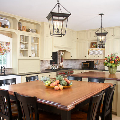 Inspiration for a timeless eat-in kitchen remodel in Boston with a farmhouse sink, shaker cabinets, yellow cabinets, wood countertops, brown backsplash, stainless steel appliances and limestone backsplash