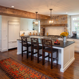 Farmhouse kitchen appliance - Inspiration for a country l-shaped dark wood floor and brown floor kitchen remodel in Philadelphia with an undermount sink, recessed-panel cabinets, white cabinets, white backsplash, subway tile backsplash, paneled appliances, an island and black countertops