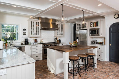 Large cottage u-shaped brick floor and multicolored floor kitchen photo in Other with a farmhouse sink, shaker cabinets, granite countertops, white backsplash, ceramic backsplash, stainless steel appliances, an island and white cabinets