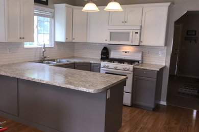 Eat-in kitchen - mid-sized contemporary u-shaped laminate floor eat-in kitchen idea in Grand Rapids with a double-bowl sink, flat-panel cabinets, white cabinets, granite countertops, white backsplash, subway tile backsplash, white appliances and a peninsula