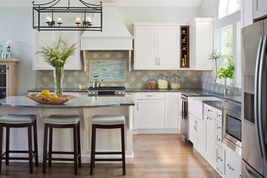Example of a large transitional l-shaped medium tone wood floor eat-in kitchen design in Denver with a farmhouse sink, shaker cabinets, white cabinets, quartz countertops, multicolored backsplash, ceramic backsplash, stainless steel appliances and an island