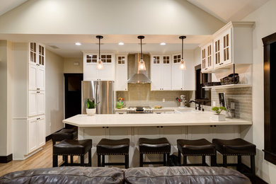 This is an example of a contemporary u-shaped open plan kitchen in Los Angeles with a belfast sink, shaker cabinets, white cabinets, quartz worktops, grey splashback, metro tiled splashback, stainless steel appliances and light hardwood flooring.