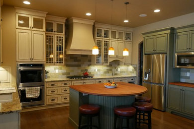 Example of a large transitional u-shaped medium tone wood floor and brown floor eat-in kitchen design in Other with an undermount sink, recessed-panel cabinets, green cabinets, wood countertops, beige backsplash, stone tile backsplash, stainless steel appliances and an island