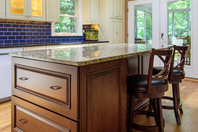 Inspiration for a mid-sized timeless l-shaped light wood floor open concept kitchen remodel in New York with an undermount sink, raised-panel cabinets, beige cabinets, granite countertops, blue backsplash, subway tile backsplash, stainless steel appliances and an island