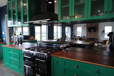 メルボルンにある高級な広いエクレクティックスタイルのおしゃれなキッチン (エプロンフロントシンク、シェーカースタイル扉のキャビネット、緑のキャビネット、木材カウンター、メタリックのキッチンパネル、ミラータイルのキッチンパネル、黒い調理設備、コンクリートの床) の写真