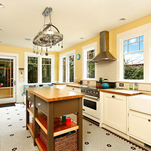 This is an example of a mid-sized victorian galley separate kitchen in Seattle with a farmhouse sink, recessed-panel cabinets, white cabinets, wood benchtops, white splashback, subway tile splashback, stainless steel appliances, ceramic floors, with island, yellow floor and brown benchtop.