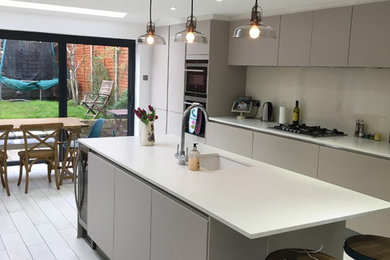 Photo of a medium sized contemporary kitchen/diner in London with an integrated sink, flat-panel cabinets, grey cabinets, composite countertops, grey splashback, glass sheet splashback, stainless steel appliances, porcelain flooring and an island.