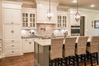 Large transitional u-shaped medium tone wood floor and brown floor kitchen photo in Other with a double-bowl sink, raised-panel cabinets, white cabinets, brown backsplash, subway tile backsplash, stainless steel appliances and an island