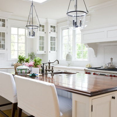 Example of a classic kitchen design in DC Metro with an undermount sink, glass-front cabinets, white cabinets and wood countertops