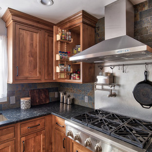 Photo of a mid-sized industrial l-shaped eat-in kitchen in New York with an undermount sink, beaded inset cabinets, medium wood cabinets, granite benchtops, grey splashback, slate splashback, stainless steel appliances, ceramic floors, with island and brown floor.