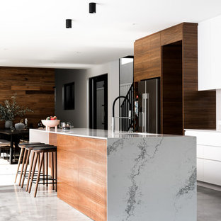 Inspiration for a large contemporary galley open plan kitchen in Perth with an undermount sink, flat-panel cabinets, white cabinets, quartz benchtops, white splashback, stone slab splashback, black appliances, concrete floors, with island and grey floor.