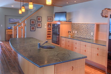 Immagine di una grande cucina minimal con lavello sottopiano, ante lisce, ante in legno chiaro, top in saponaria, paraspruzzi verde, paraspruzzi con lastra di vetro e pavimento in legno massello medio