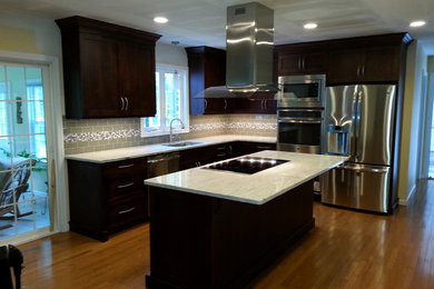 Mid-sized transitional u-shaped light wood floor eat-in kitchen photo in New York with a double-bowl sink, raised-panel cabinets, dark wood cabinets, wood countertops, gray backsplash, subway tile backsplash, stainless steel appliances and an island