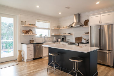 Example of a cottage l-shaped medium tone wood floor and brown floor kitchen design in Other with a farmhouse sink, recessed-panel cabinets, white cabinets, stainless steel appliances, an island and white countertops