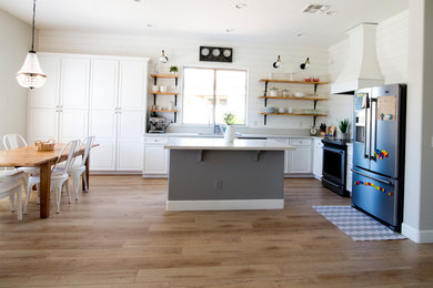 Cette photo montre une grande cuisine américaine nature en U avec un évier encastré, un placard avec porte à panneau surélevé, des portes de placard blanches, un plan de travail en quartz, une crédence blanche, une crédence en bois, un électroménager en acier inoxydable, sol en stratifié et un sol marron.