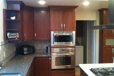 Cette image montre une cuisine américaine en bois brun avec un placard avec porte à panneau encastré, une crédence grise, un électroménager en acier inoxydable et un sol en bois brun.