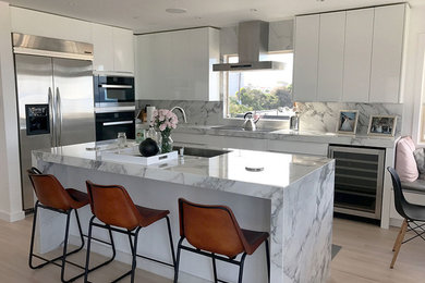 Example of a large minimalist l-shaped light wood floor and beige floor open concept kitchen design in Los Angeles with flat-panel cabinets, white cabinets, multicolored backsplash, porcelain backsplash, stainless steel appliances and an island