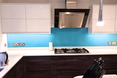 This is an example of a medium sized contemporary u-shaped enclosed kitchen in Berkshire with quartz worktops, blue splashback, glass sheet splashback, stainless steel appliances, an island and white worktops.