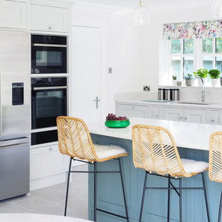 This is an example of a traditional l-shaped kitchen in Kent with a submerged sink, shaker cabinets, blue cabinets, grey splashback, stainless steel appliances, an island, grey floors and white worktops.