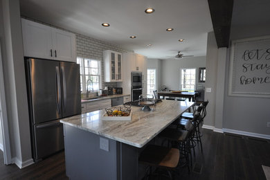 Example of a mid-sized farmhouse brown floor eat-in kitchen design in Atlanta with white cabinets, granite countertops, white backsplash, stainless steel appliances and an island