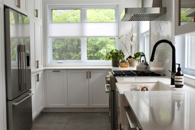 Kitchen - mid-sized 1950s u-shaped ceramic tile and gray floor kitchen idea in Montreal with a farmhouse sink, shaker cabinets, white cabinets, quartz countertops, white backsplash, ceramic backsplash, stainless steel appliances, a peninsula and white countertops