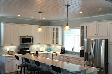 Example of a mid-sized classic l-shaped dark wood floor and brown floor eat-in kitchen design in Orlando with an undermount sink, shaker cabinets, white cabinets, quartzite countertops, glass tile backsplash, stainless steel appliances, an island, gray backsplash and white countertops