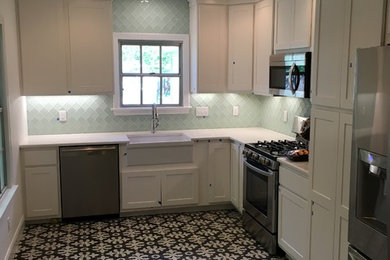Inspiration for a mid-sized eclectic l-shaped porcelain tile and multicolored floor enclosed kitchen remodel in Austin with a farmhouse sink, green backsplash, glass tile backsplash, stainless steel appliances, shaker cabinets, white cabinets, solid surface countertops and no island