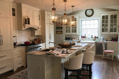 This is an example of a medium sized farmhouse l-shaped enclosed kitchen in DC Metro with a submerged sink, shaker cabinets, white cabinets, marble worktops, white splashback, metro tiled splashback, integrated appliances, medium hardwood flooring, an island and brown floors.