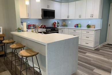 Example of a mid-sized transitional u-shaped vinyl floor and gray floor eat-in kitchen design in Orange County with a farmhouse sink, shaker cabinets, white cabinets, marble countertops, white backsplash, stainless steel appliances, a peninsula and white countertops