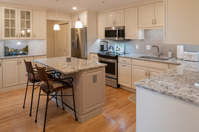Inspiration for a medium sized traditional l-shaped enclosed kitchen in Boston with a submerged sink, raised-panel cabinets, white cabinets, engineered stone countertops, beige splashback, metro tiled splashback, stainless steel appliances, light hardwood flooring, an island, brown floors and grey worktops.