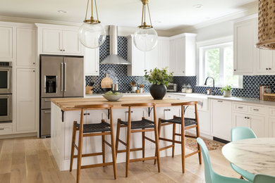Trendy l-shaped light wood floor and beige floor eat-in kitchen photo in Boston with a farmhouse sink, white cabinets, blue backsplash, ceramic backsplash, recessed-panel cabinets, stainless steel appliances and an island