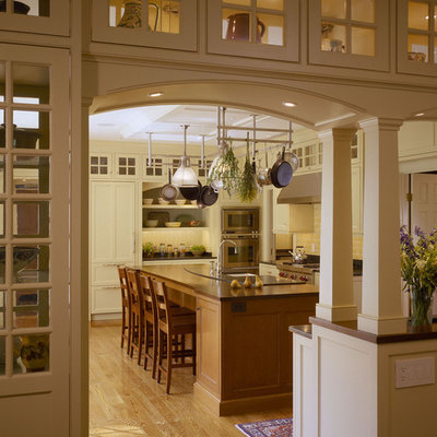 Inspiration for a mid-sized timeless u-shaped medium tone wood floor eat-in kitchen remodel in Boston with white cabinets, white backsplash, recessed-panel cabinets, solid surface countertops, stone tile backsplash, stainless steel appliances, an island and a farmhouse sink