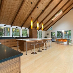 This is an example of a large contemporary l-shaped eat-in kitchen in Boston with flat-panel cabinets, medium wood cabinets, soapstone benchtops, black splashback, slate splashback, panelled appliances, light hardwood floors and with island.
