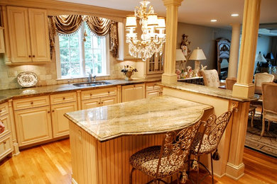 Inredning av ett klassiskt mellanstort kök, med en dubbel diskho, luckor med upphöjd panel, beige skåp, granitbänkskiva, beige stänkskydd, stänkskydd i keramik, rostfria vitvaror, mellanmörkt trägolv och en köksö